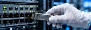 A gloved technician inserting an optical transceiver into a network switch for a compatibility check